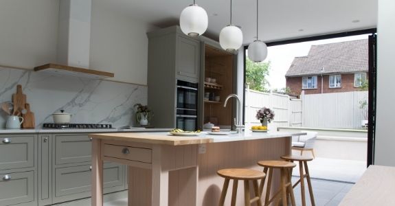 three pane aluminium bifold door bringing light into a pastel coloured kitchen extension