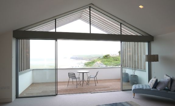 slim sliders with fixed glazing and gable end windows leading to a balcony with a sea view
